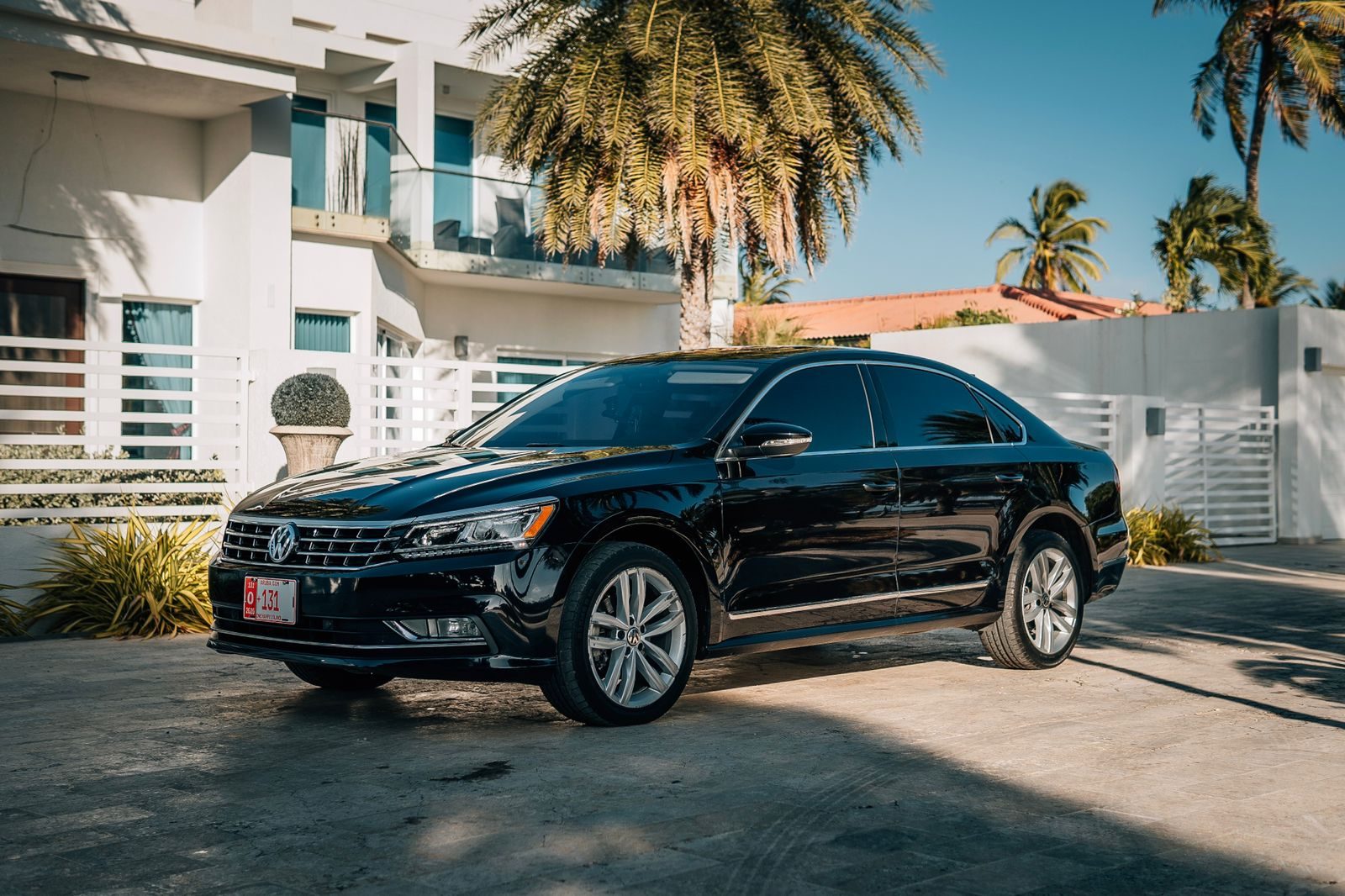 Black Volkswagen Passat parked in front of a white villa with palm trees in Aruba